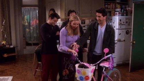 Ross gives Phoebe a bike styled for a little kid as a gift and her mouth is open with shock/happiness
