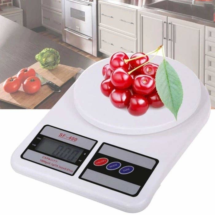 A white electronic weighing scale with a bunch of cherries kept on it