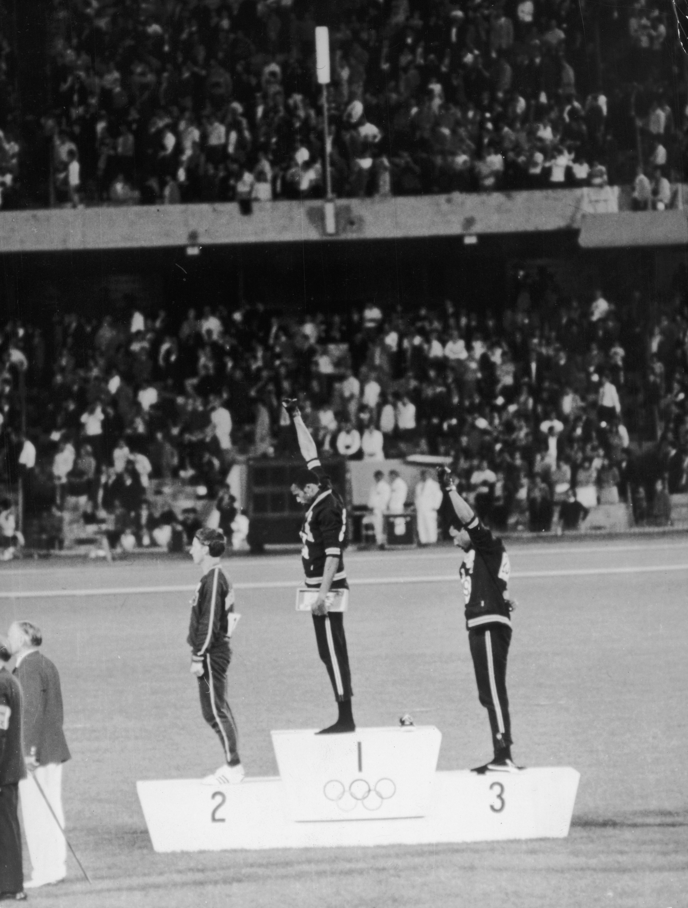 Tommie Smith and John Carlos raise their fist in the air while standing on the podium