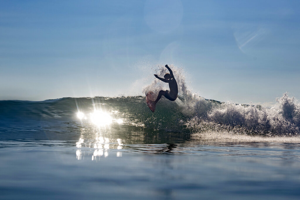 John John surfing, suspended in air, with sunlight hitting the water