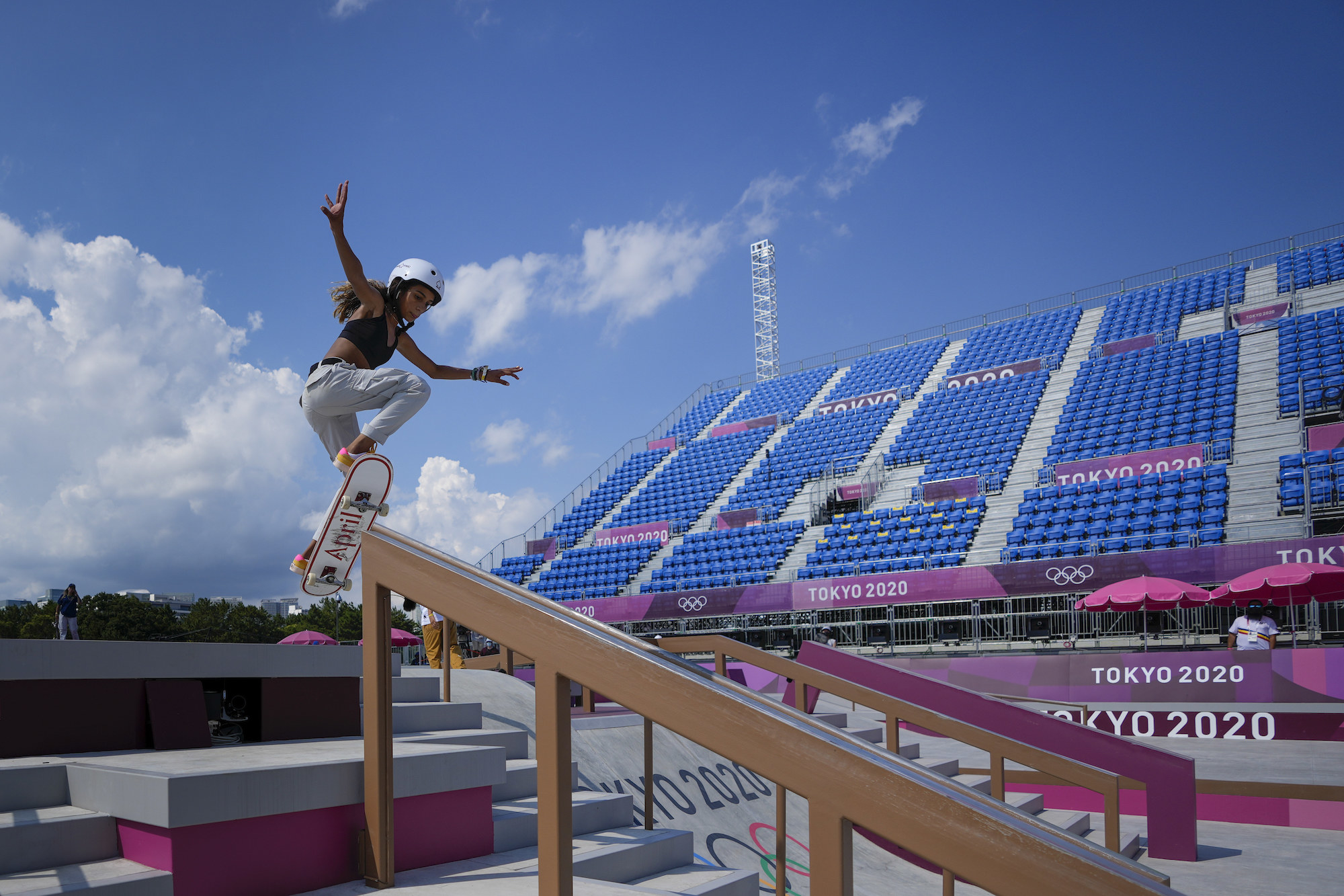 A helmeted Rayssa skateboarding down a stair handrail, arms raised