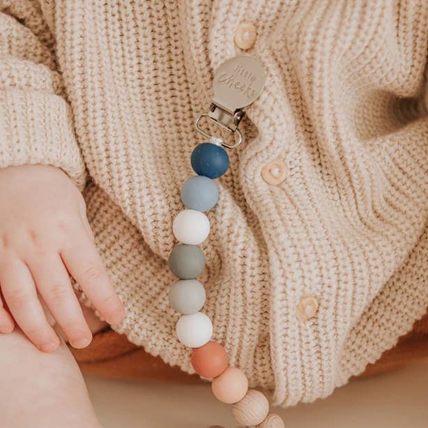 A baby wearing a cardigan with a pacifier clip attached to it