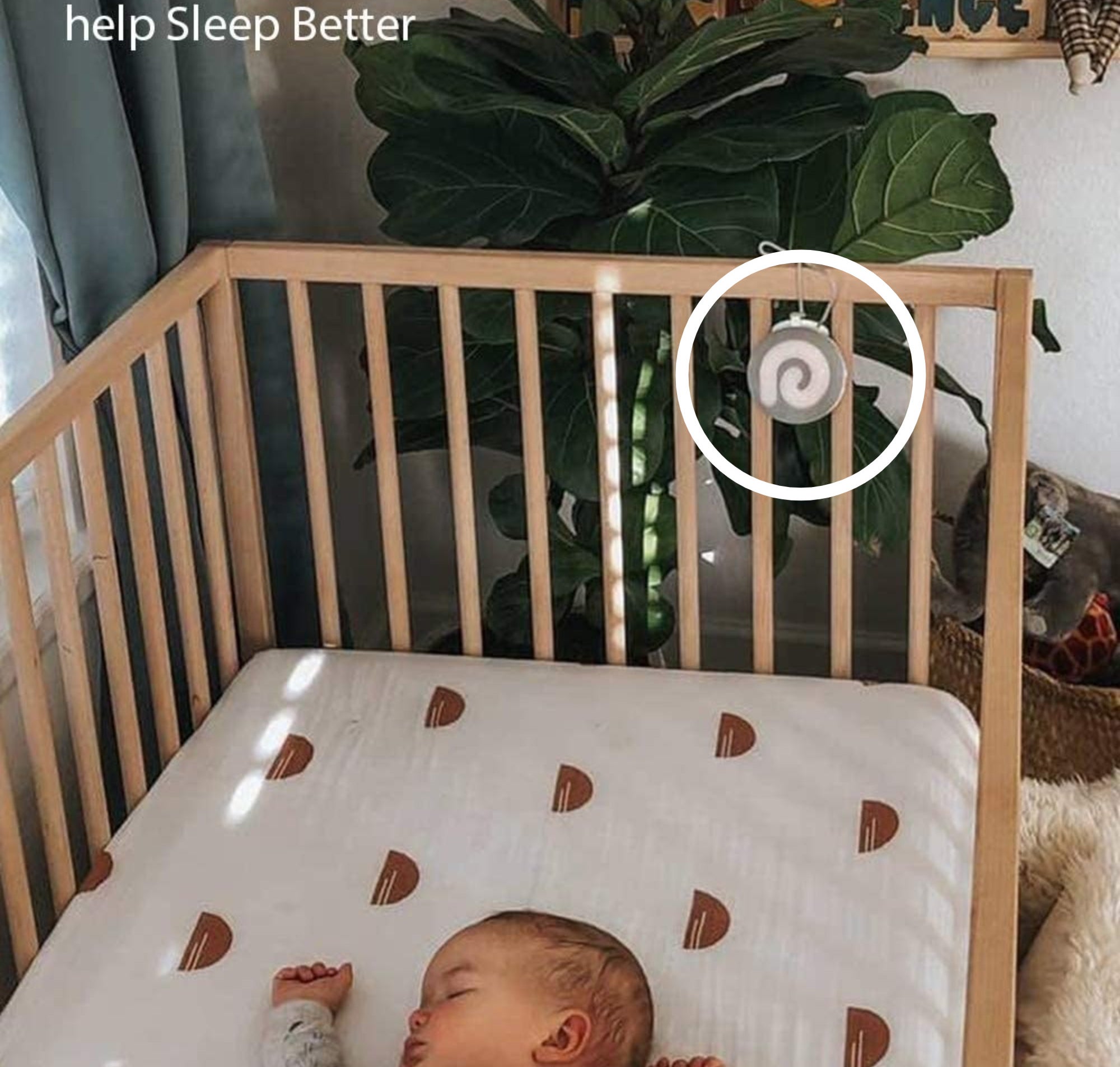 A baby sleeping in a crib with a small sound machine hanging from the edge of the crib