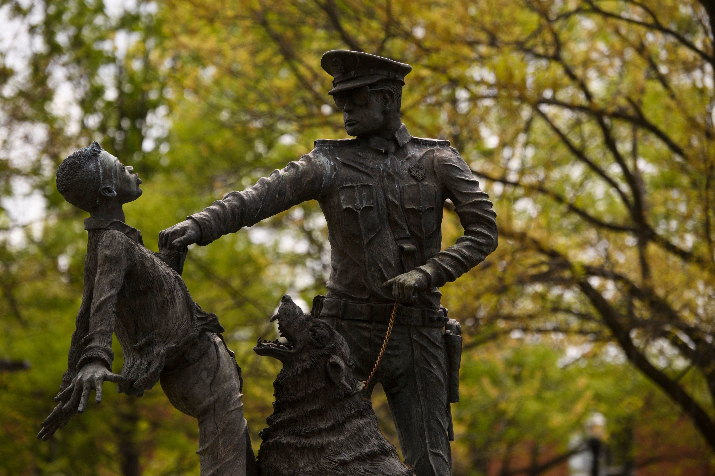 Statue of a police man and an aggressively barking dog holding on to the shirt of a small African American boy