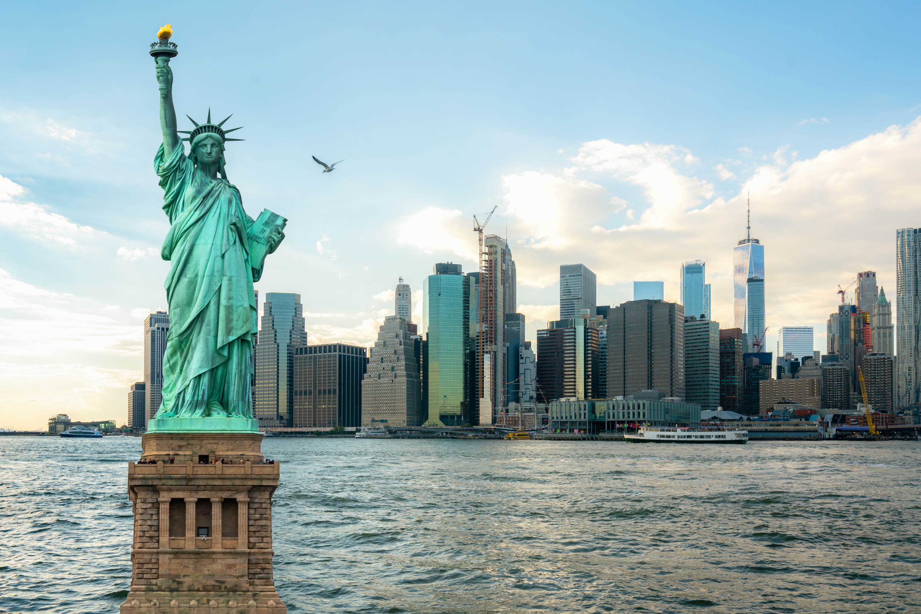 The Statue of Liberty towers over the Hudson, with a bird flying in the background, as well as many skyscrapers