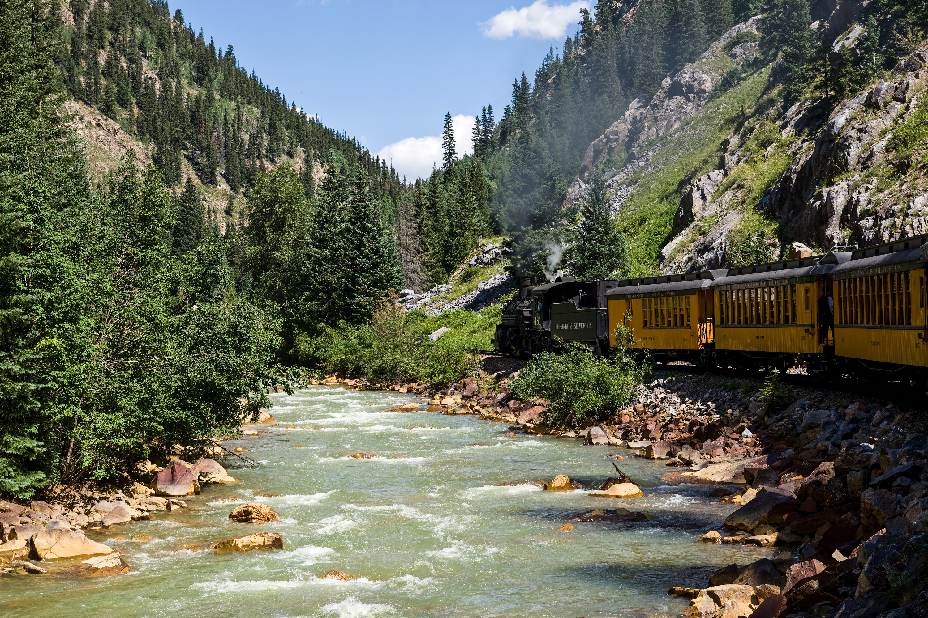 A train passes by a river in the mountains