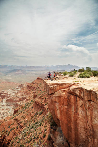 Couple with bicycles on cliff against cloudy sky