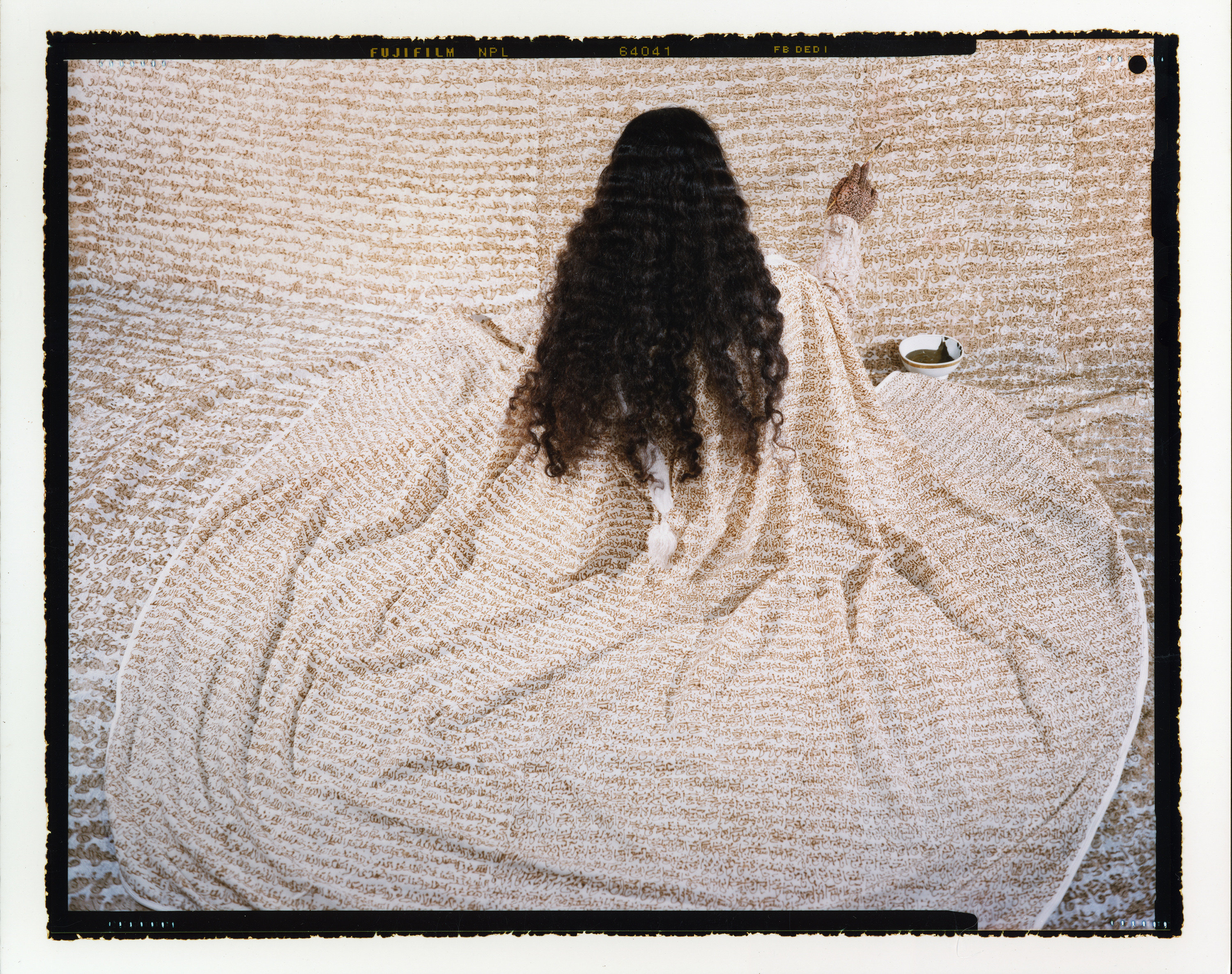A long-haired woman in a robe paints a wall with the same pattern