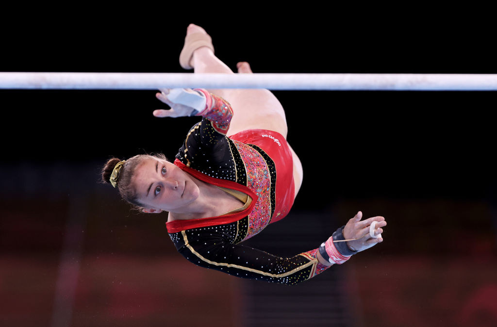 A gymnast reaching for the bar with one hand