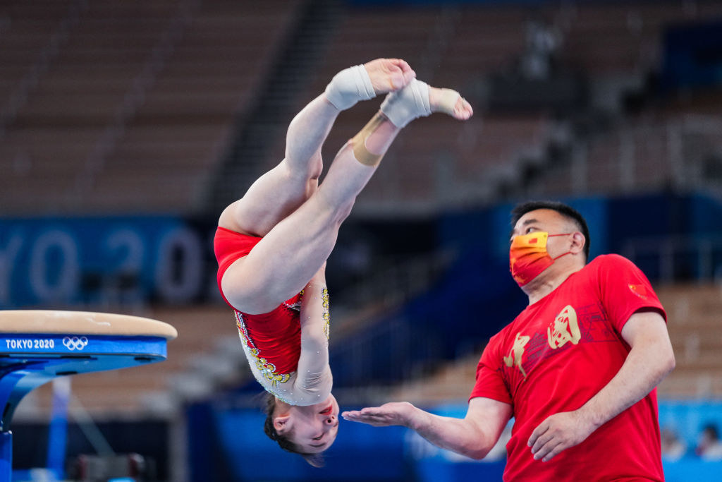 A man with his palm extended as a gymnast attempts to land