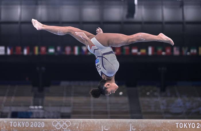 A gymnast airborne and upside down doing the splits over the balance beam