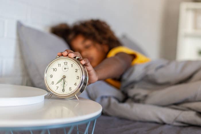 A girl turning off an alarm clock while lying in bed.