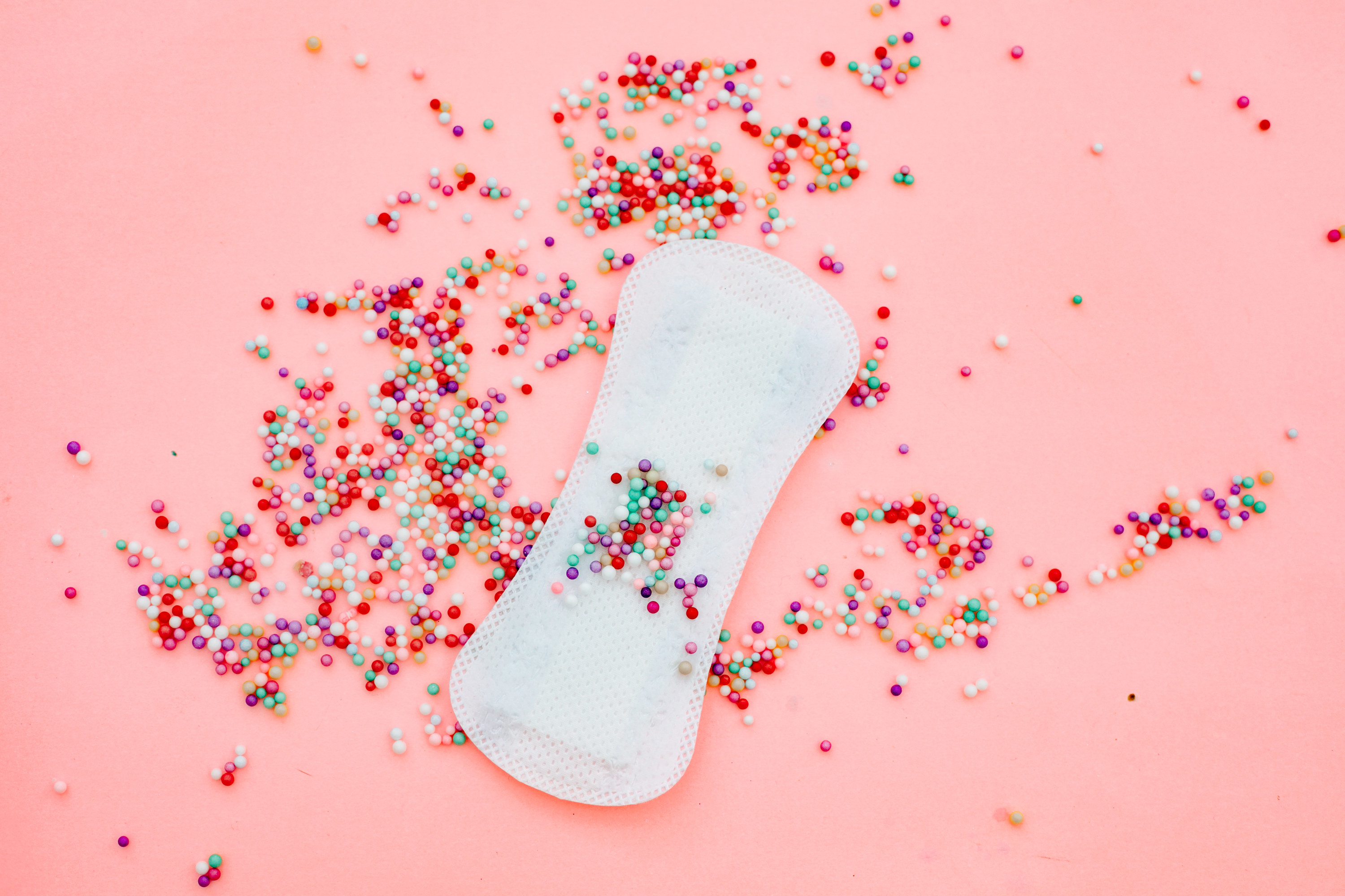 An image of a menstrual pad on a pink background with sprinkles all over