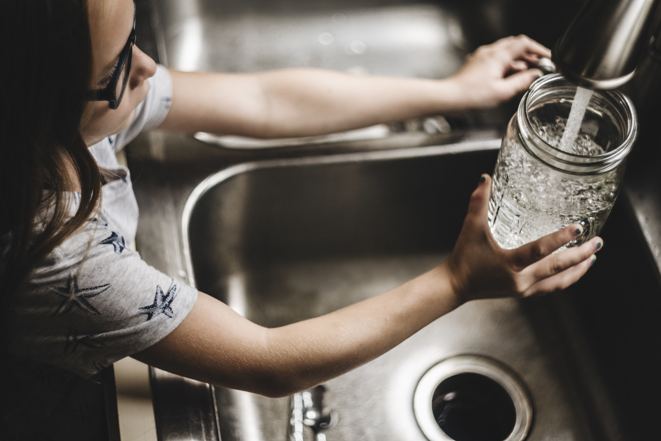 A young girl filling a mason jar from the tap