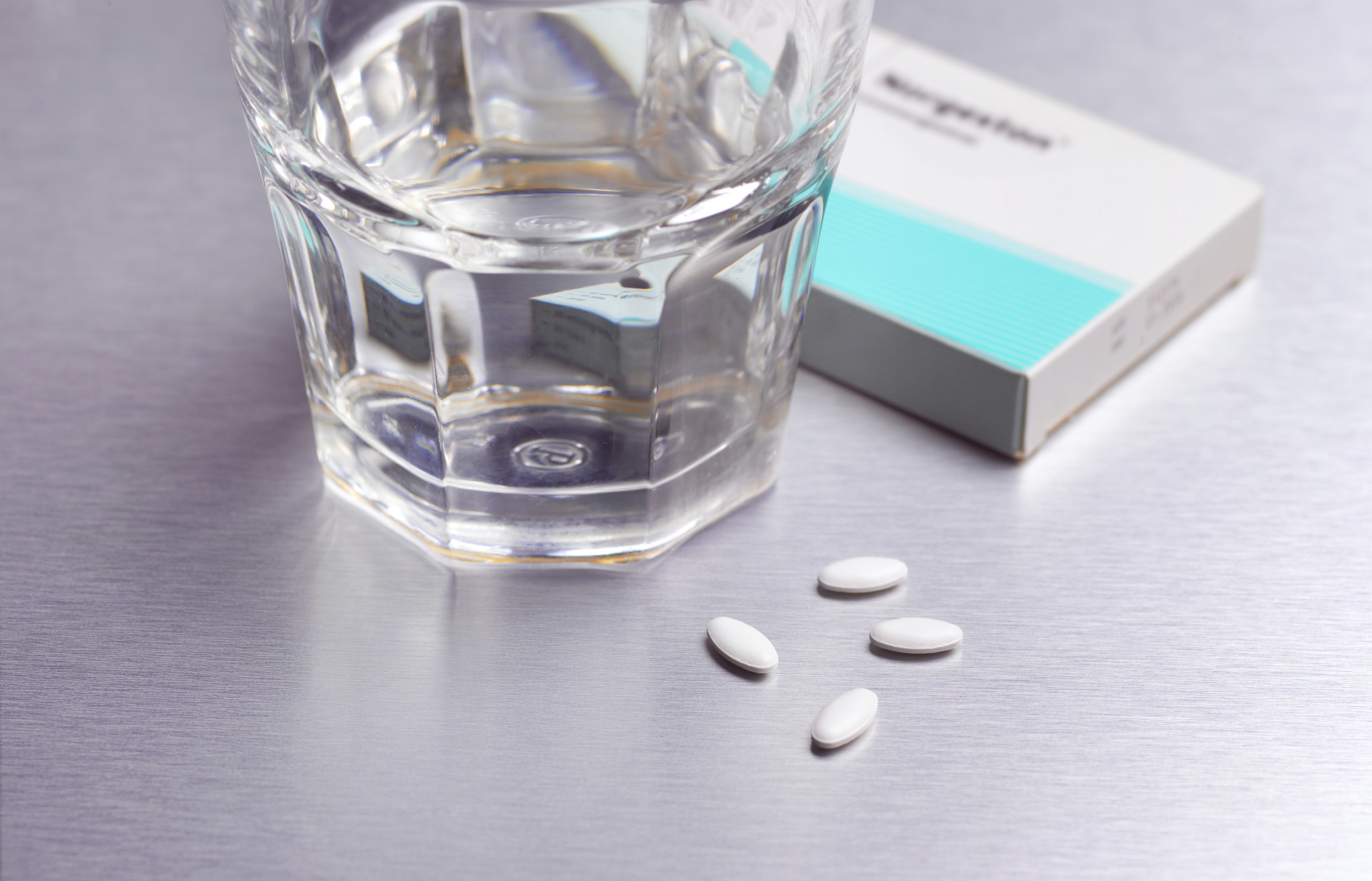 An image of four tablets on a table next to a glass of water