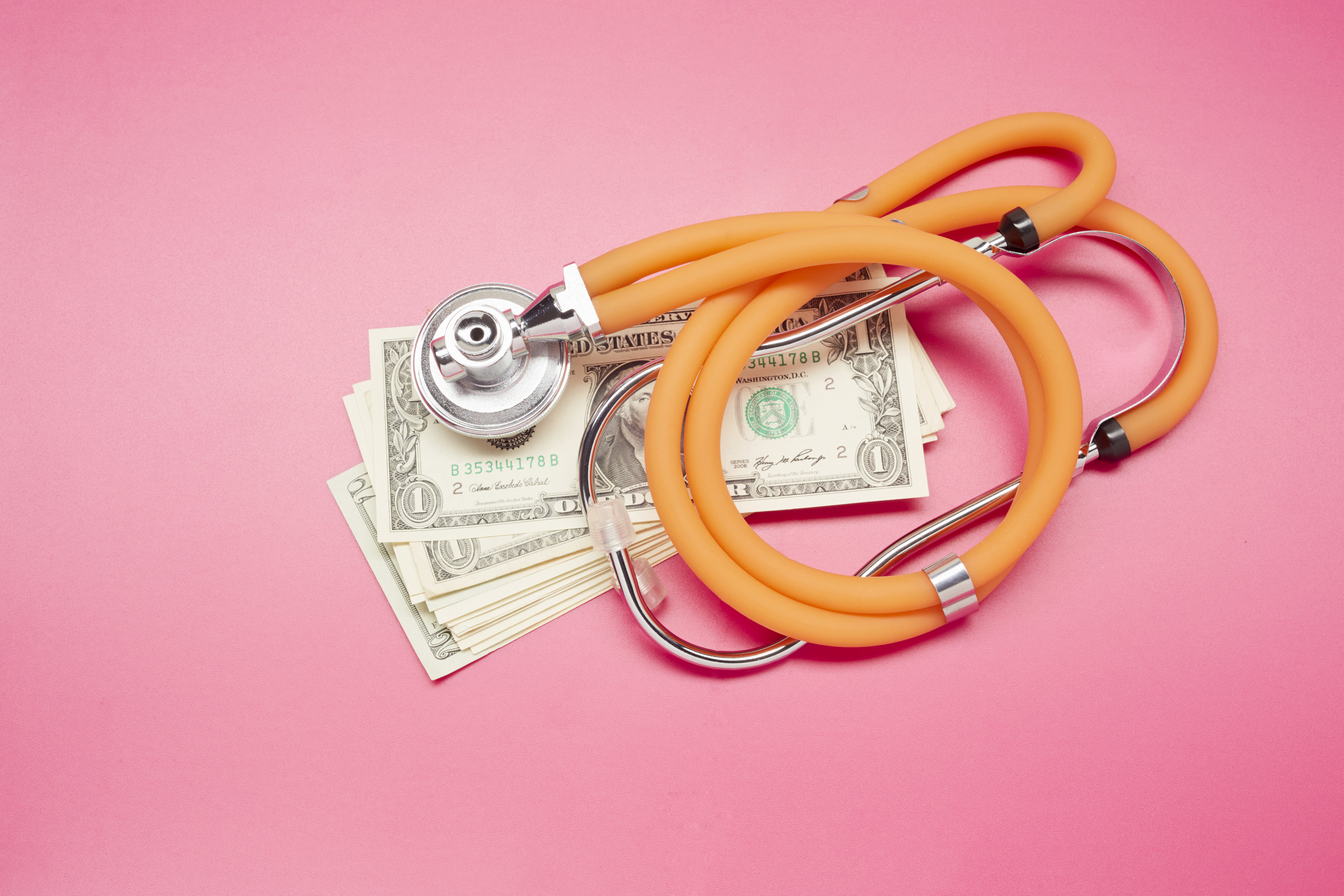 An image of a stethoscope on top of a pile of money on a pink background