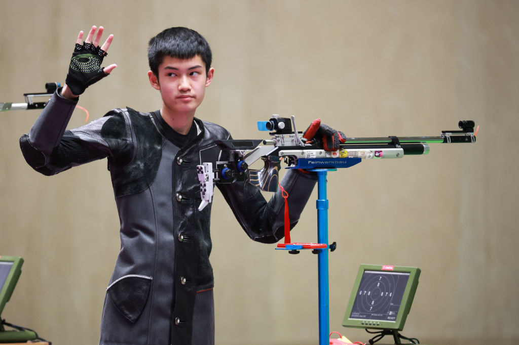 Sheng Lihao waving as he stands next to his air rifle
