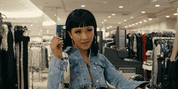 Constance Wu in Hustlers holds up a credit card at a cashier and raises her eyebrows as the camera zooms in