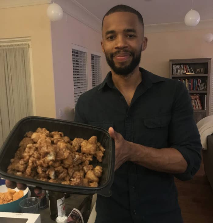 A guy holding a large container of orange chicken