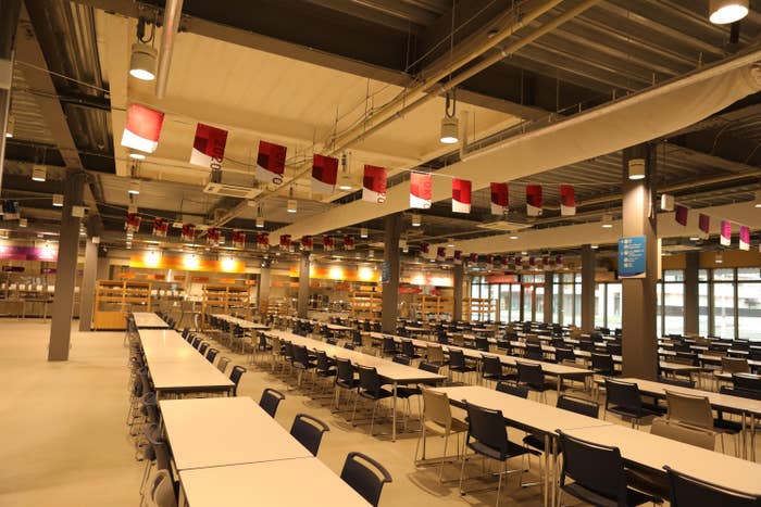 A empty dining hall features rows of empty tables in a cafeteria setting