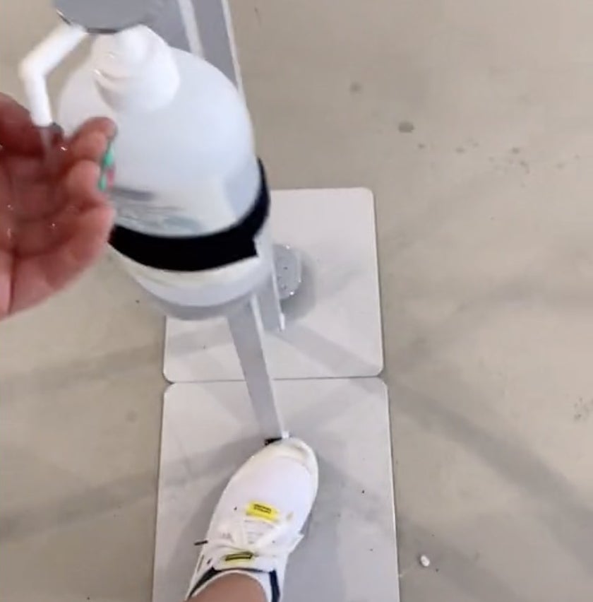A foot presses down on a button to dispense hand sanitizer into an open hand