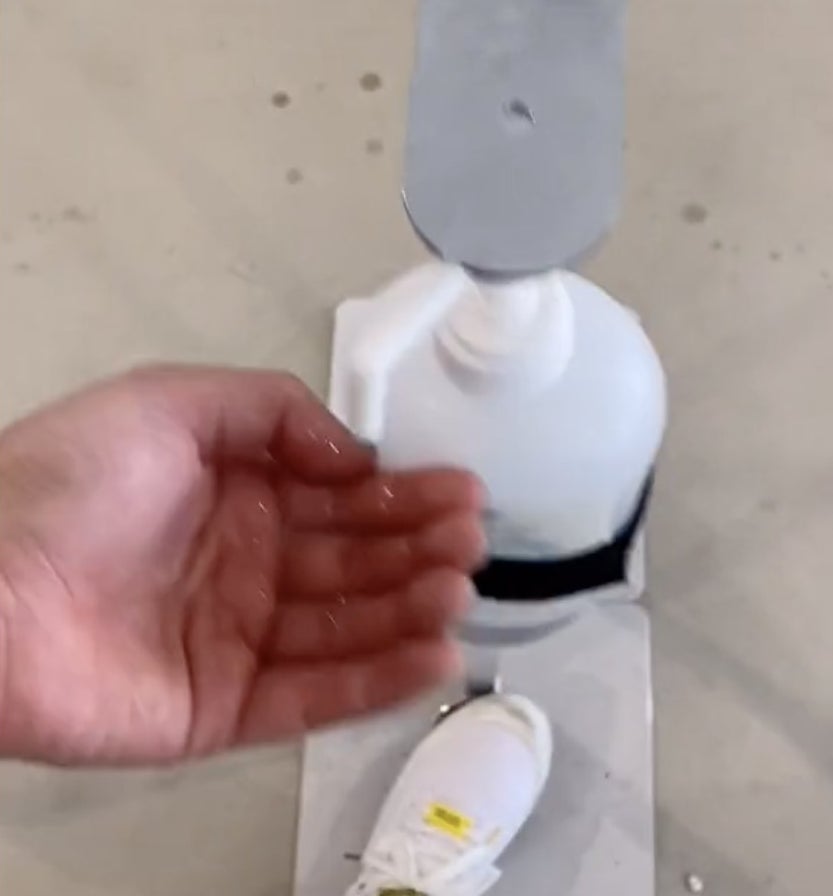 A foot presses down on a button to dispense hand sanitizer into an open hand