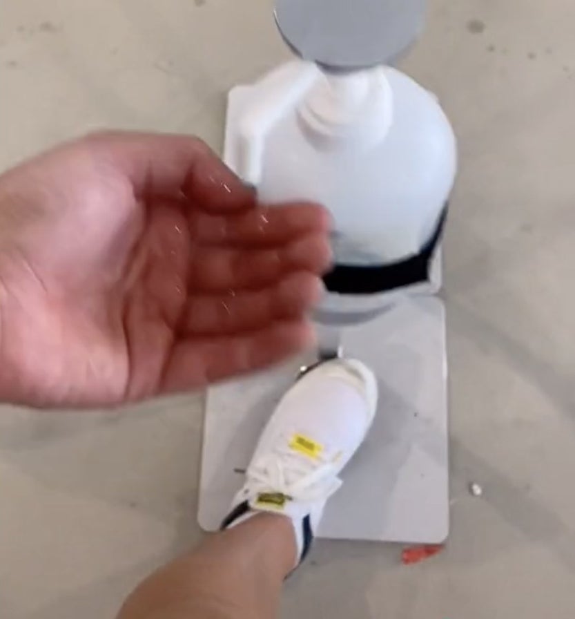 A foot presses down on a button to dispense hand sanitizer into an open hand