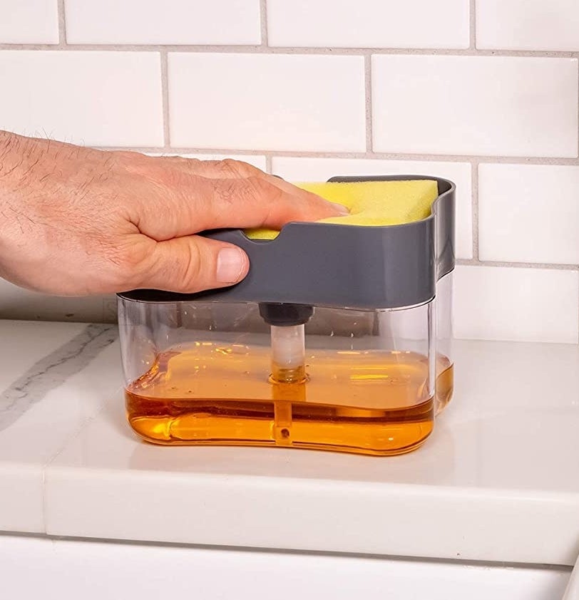A person pressing a sponge on the top of the soap-filled dispenser.