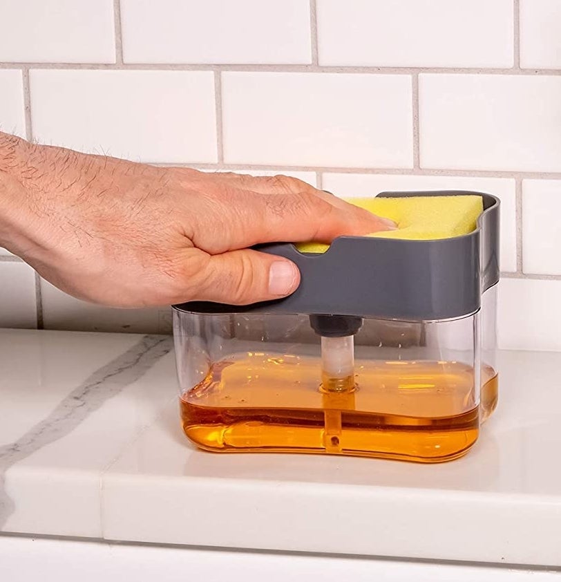 A person pressing a sponge on the top of the soap-filled dispenser.