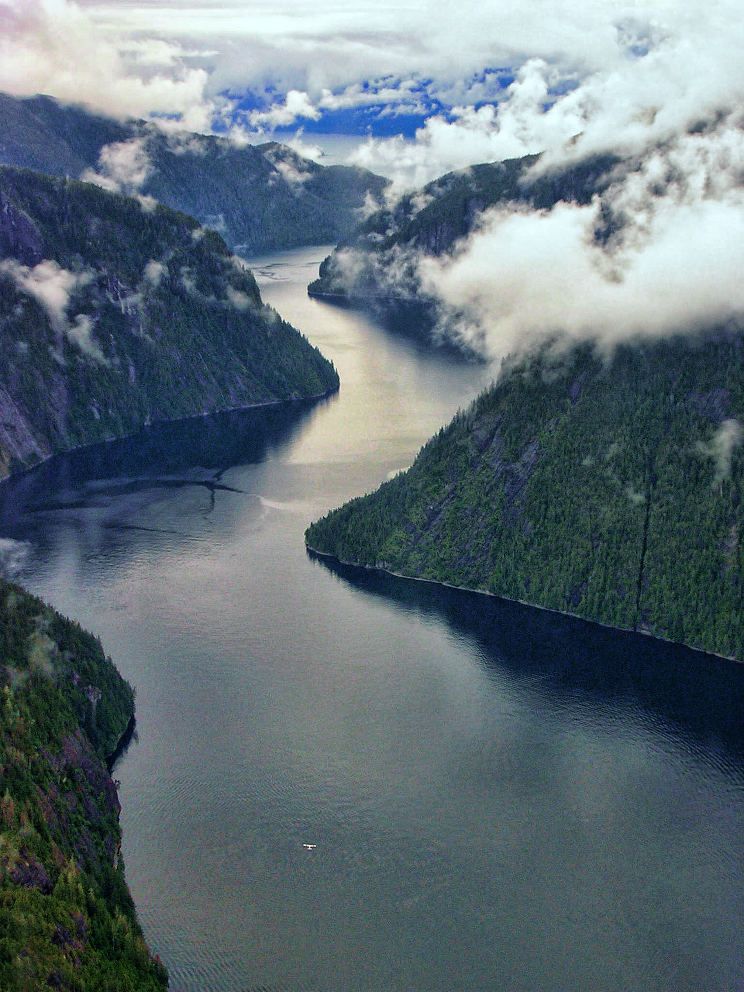 A view of Misty Fjords&#x27; mountain peaks with a body of water cutting through it and fog enveloping the view