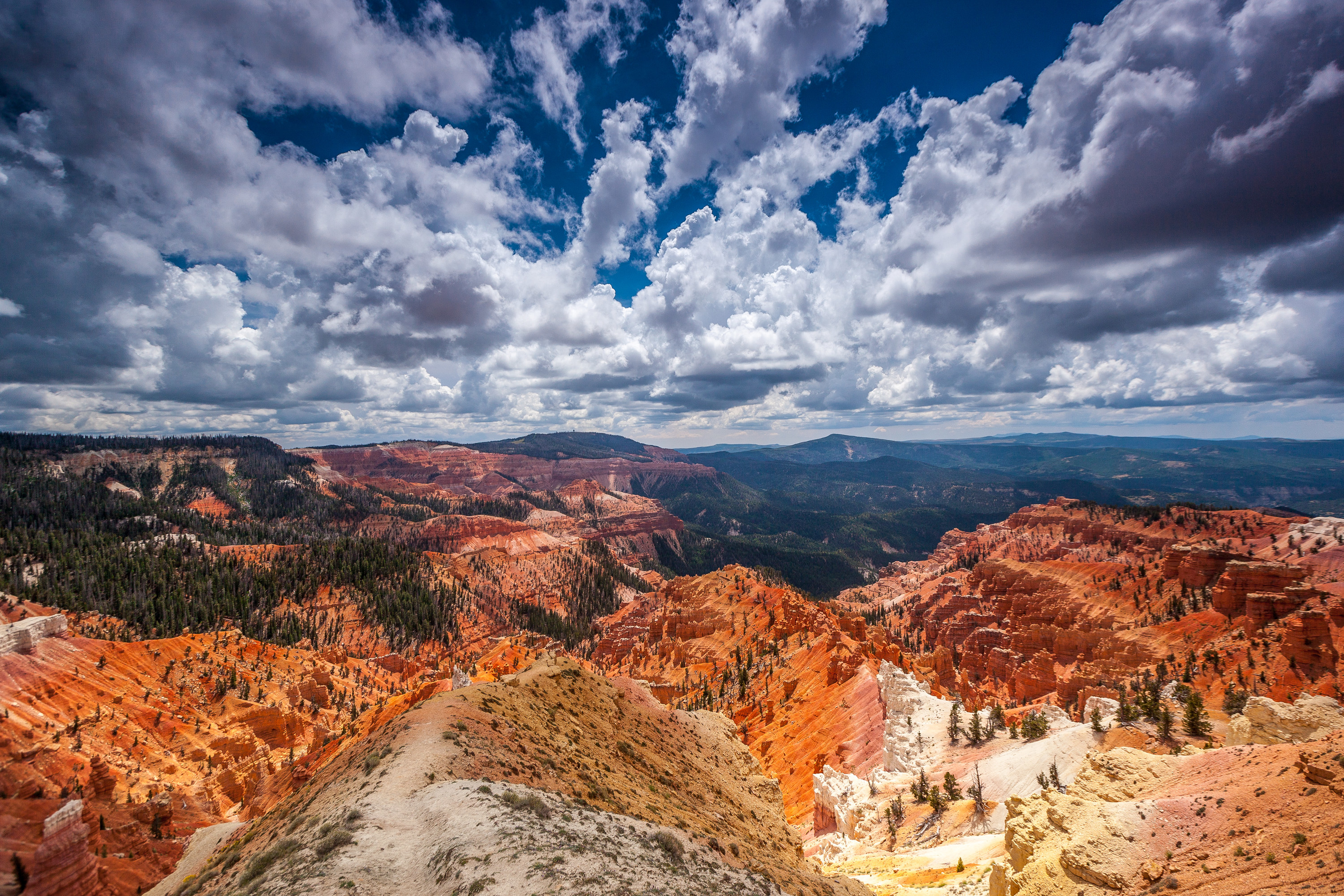 A view from a high point of Cedar Breaks National Monument shows jagged hills and rocks. In the middle, a large geologic amphitheater swoops down