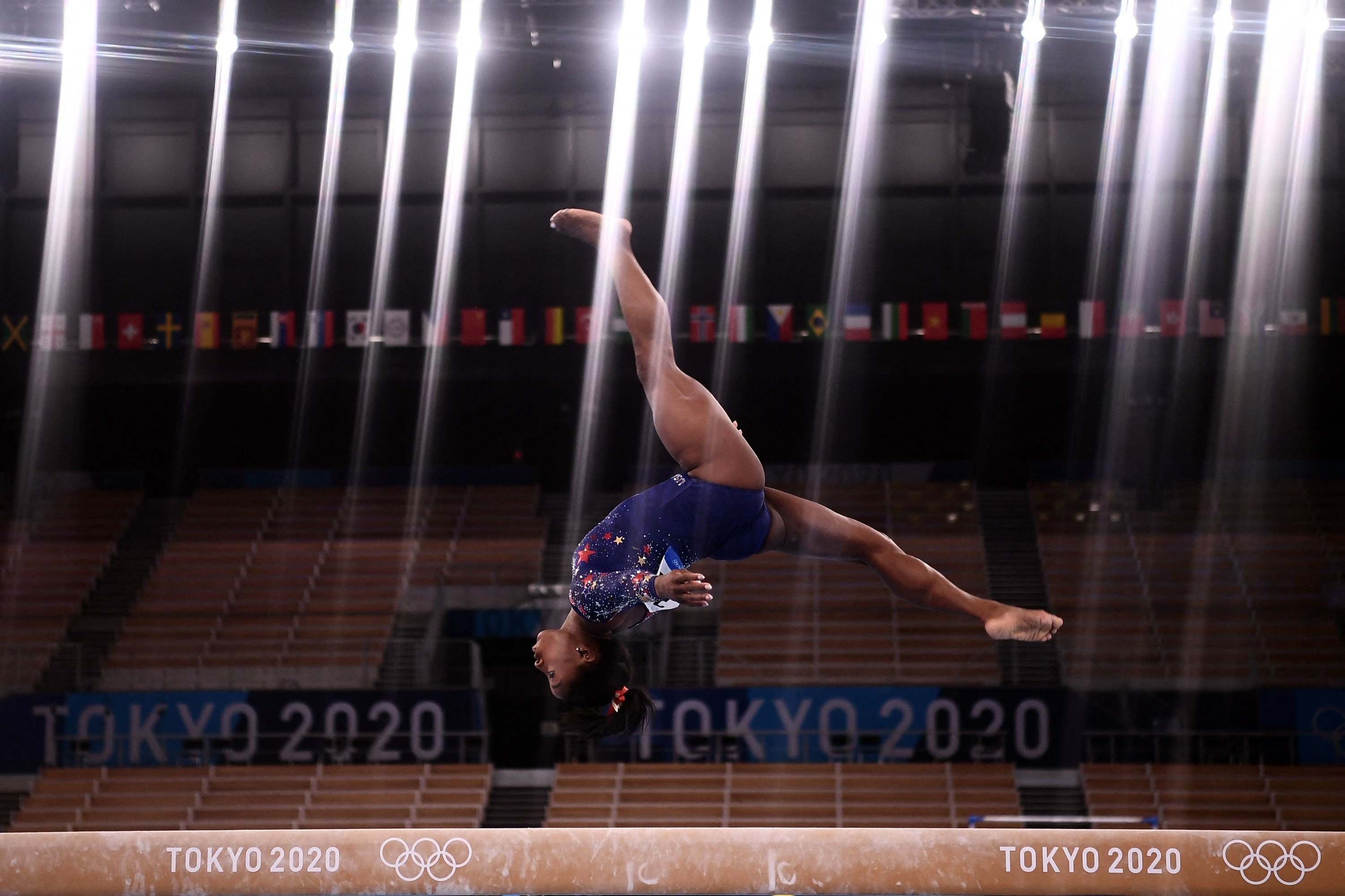 The overhead lights in the arena shining down as Simone flips over the balance beam