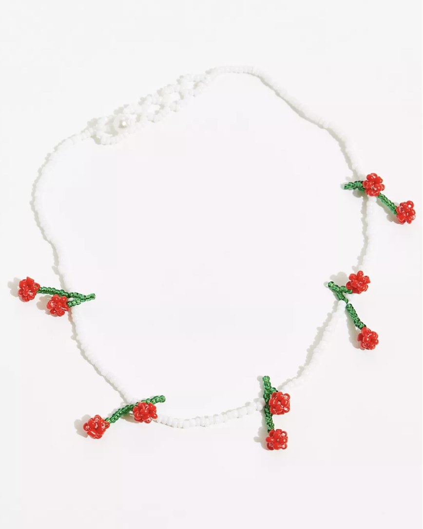 a white beaded necklace with red and green beaded floral charms