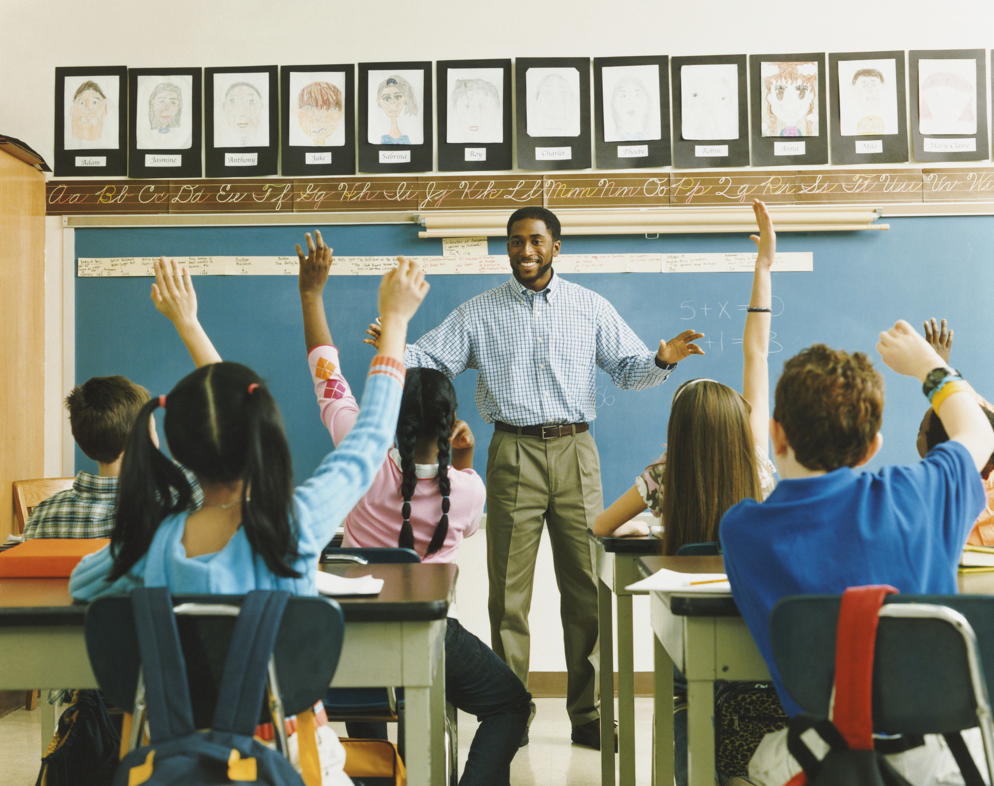 teacher in front of a class of students raising their hands