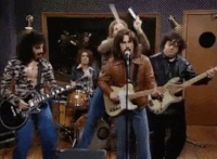 gif of will ferrel in the snl &quot;more cowbell&quot; sketch dancing and playing a cowbell with gusto with a band