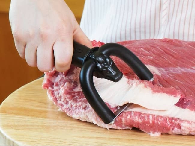 Hand using the black meat trimmer to shave a sliver of fat from a large hunk of meat