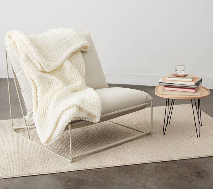 the cream throw over a chair next to a side table with books