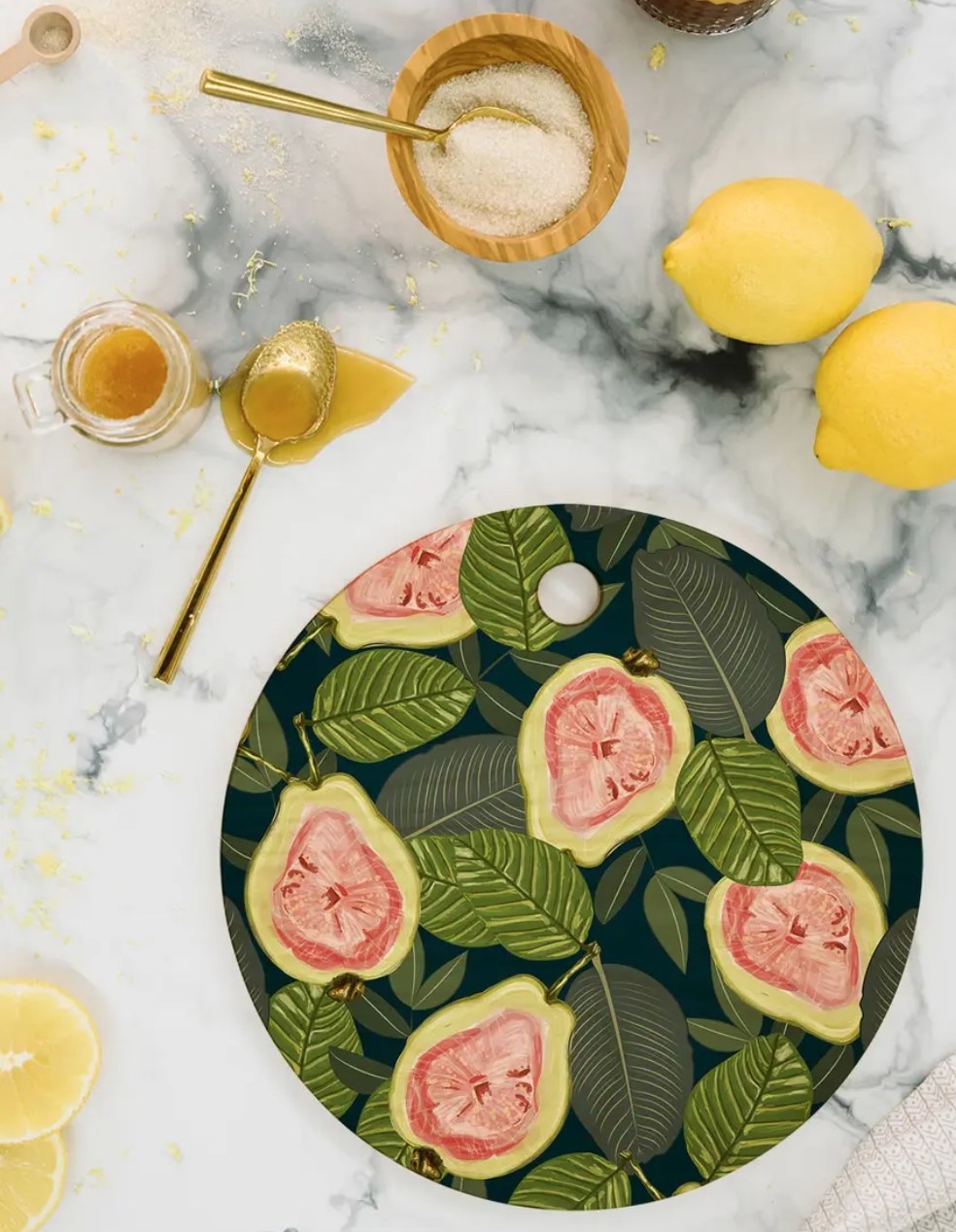 the cutting board with leaves and halved guavas on a counter next to lemons and honey