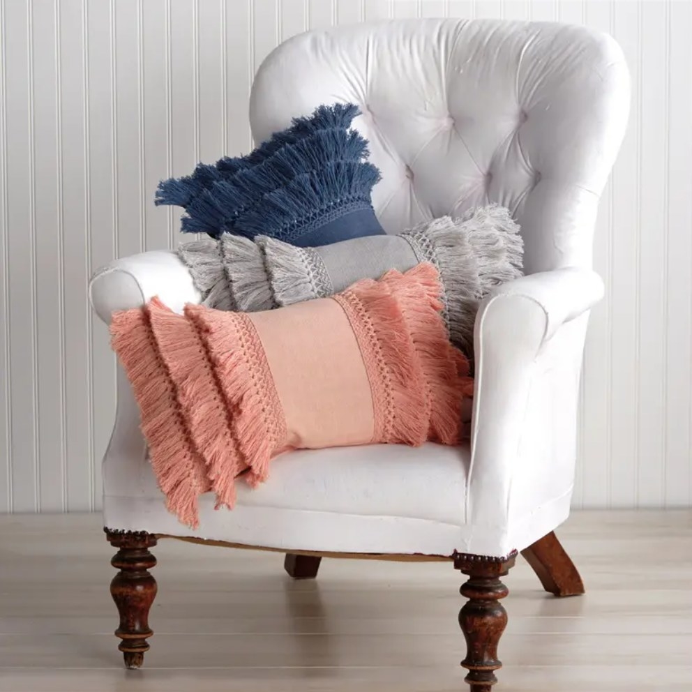 three of the fringe pillows in pink, navy, and gray