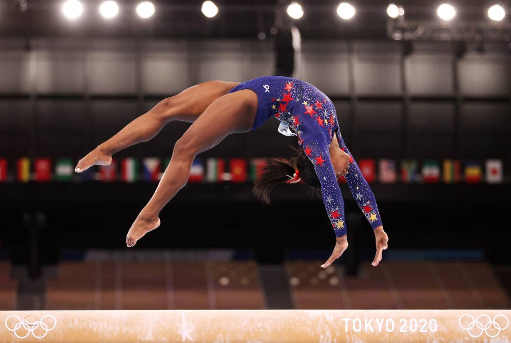 Simone Biles of Team United States competes in the Olympics, shown upside down midflip on a balance beam