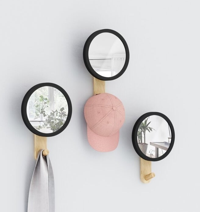 A trio of circular mirrors with wooden hooks hung on a wall