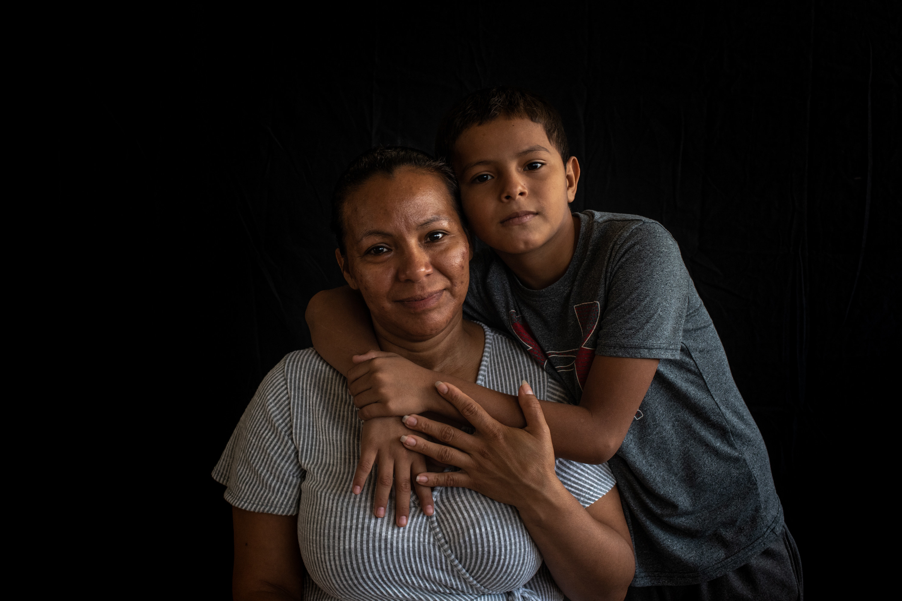 A son hods his mother from behind as they both look into the camera