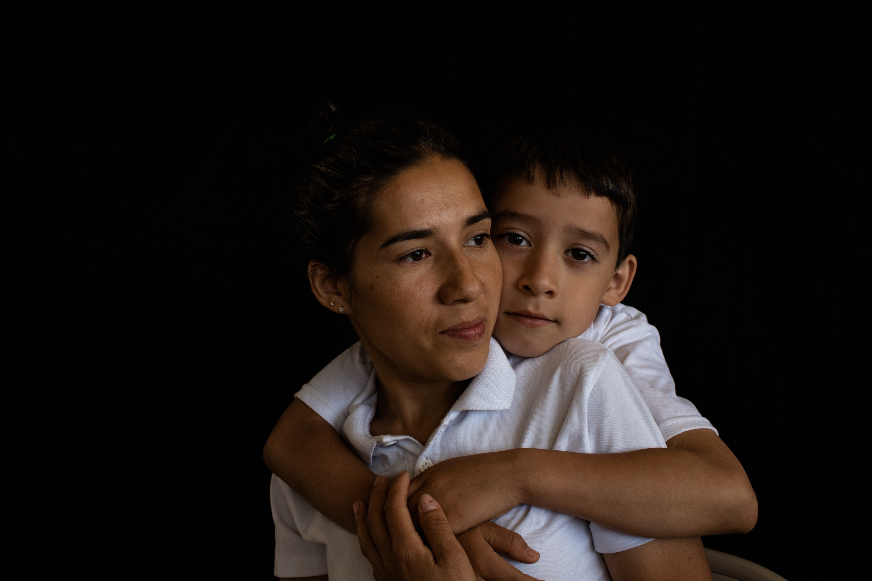 A sitting woman is held by her son, who stands behind her and embraces her