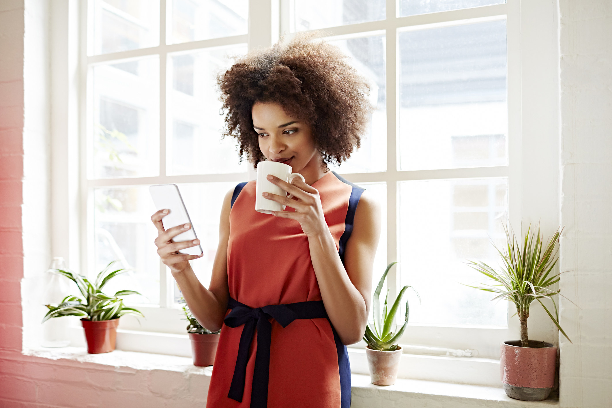 Woman sips coffee while browsing through phone