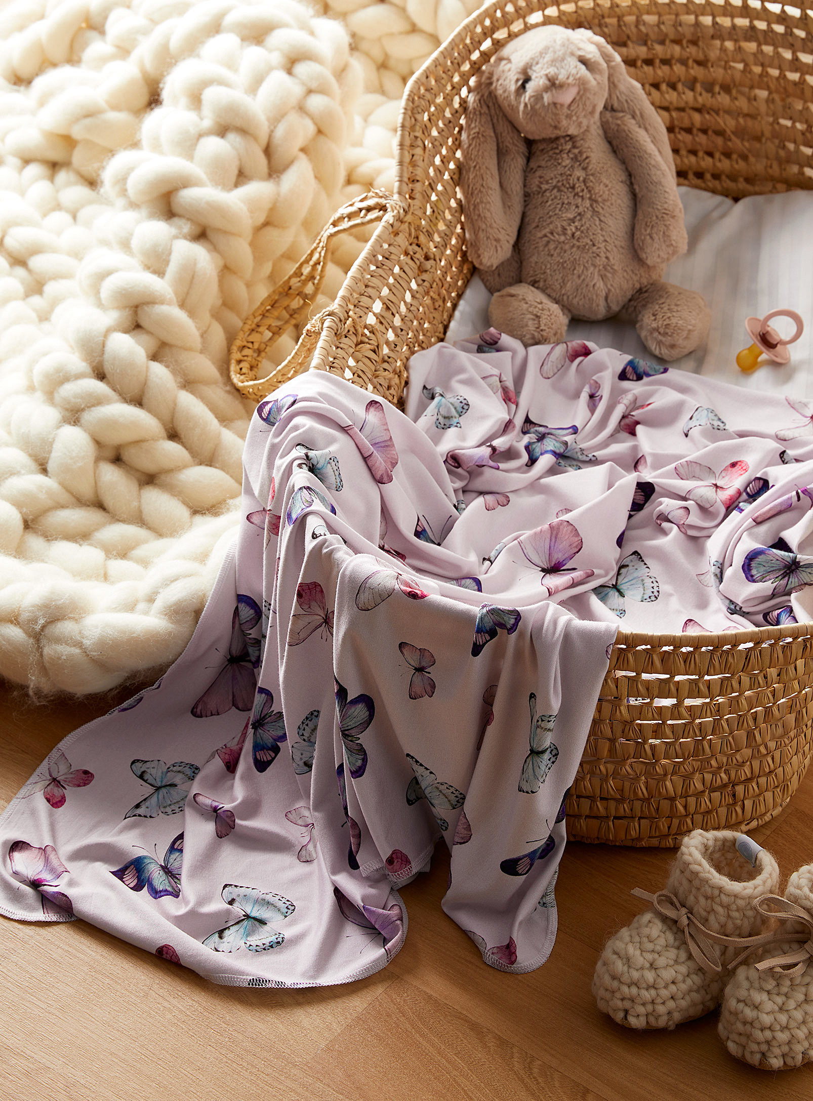 A blanket with a butterfly print lying in a woven straw bassinet