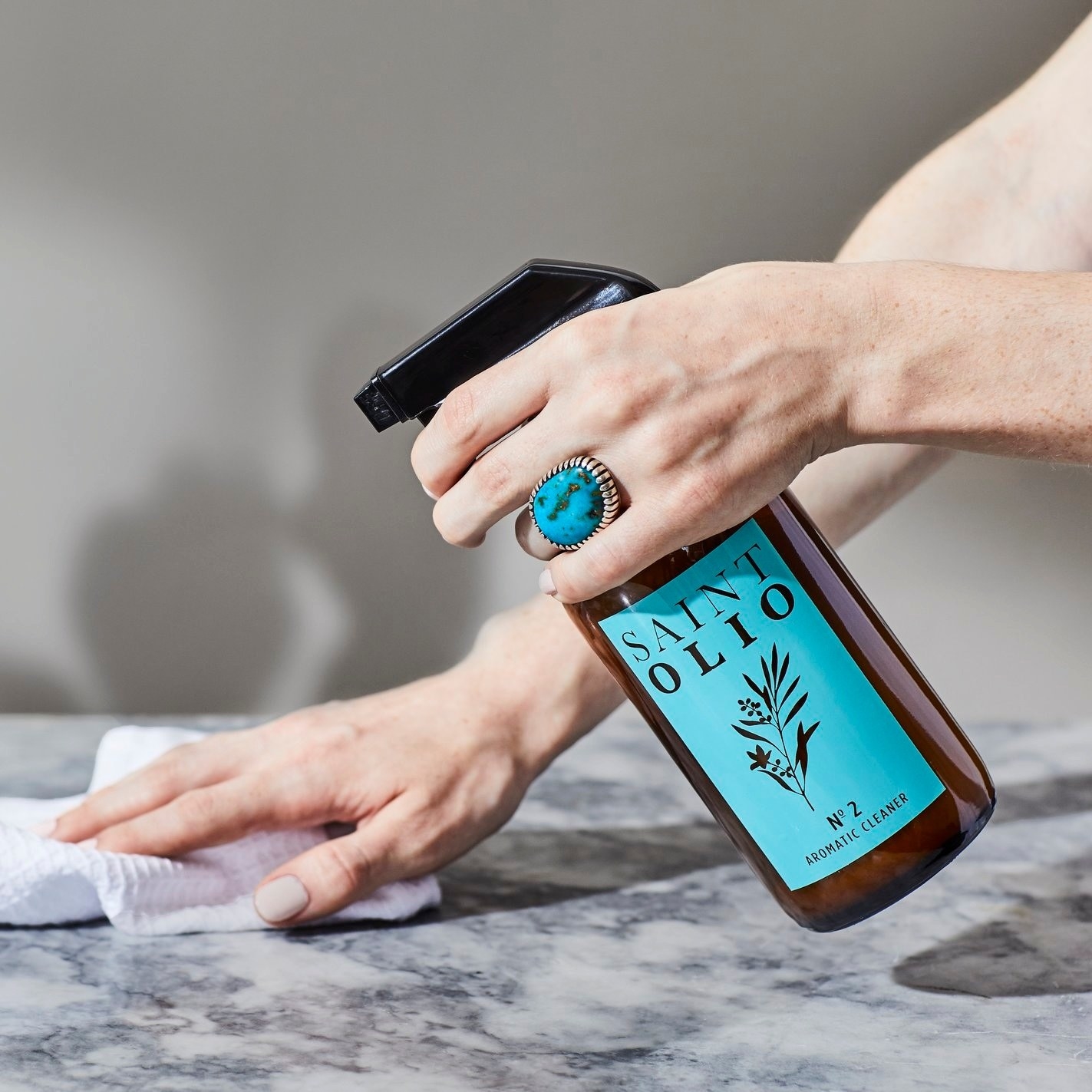 A person's hand uses a bottle of the cleaner to clean a marble surface
