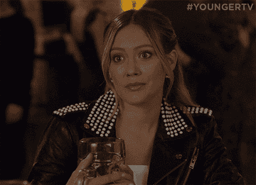GIF of Hilary Duff on Younger holding a glasses of wine and giving awkward glances