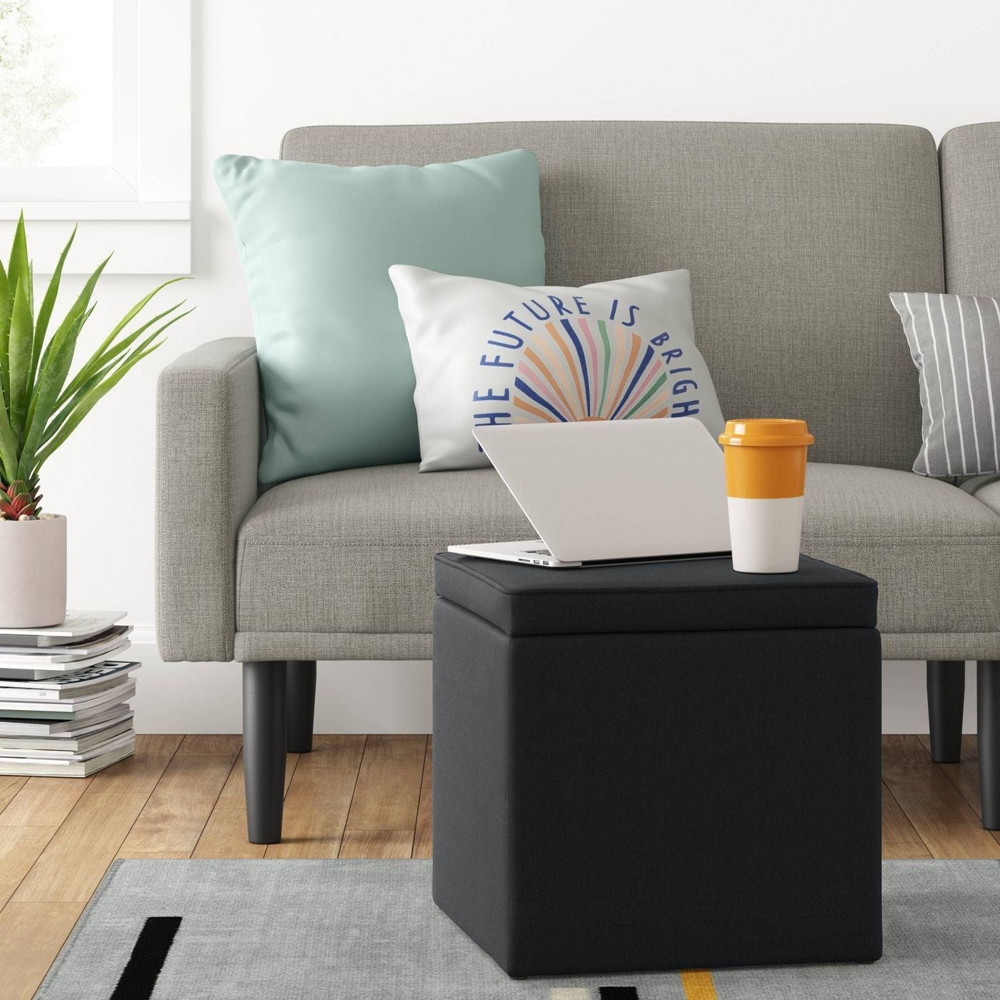 a black ottoman in a living room with a laptop and coffee tumbler on top