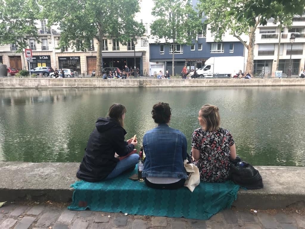 Three women sit by the water