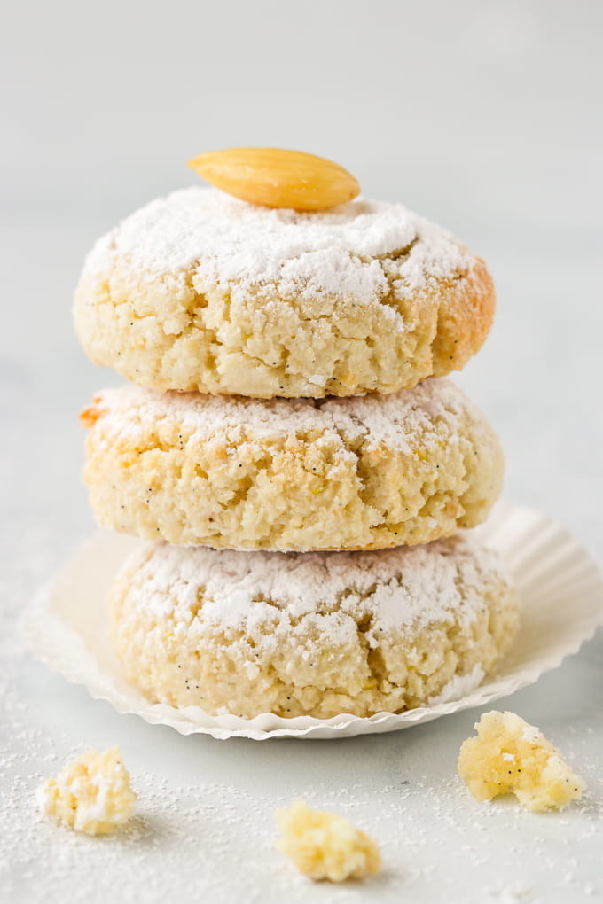 Crumbly, soft, and plush ricciarelli cookies dusted with sugar. On top of the stack of three cookies is a single almond
